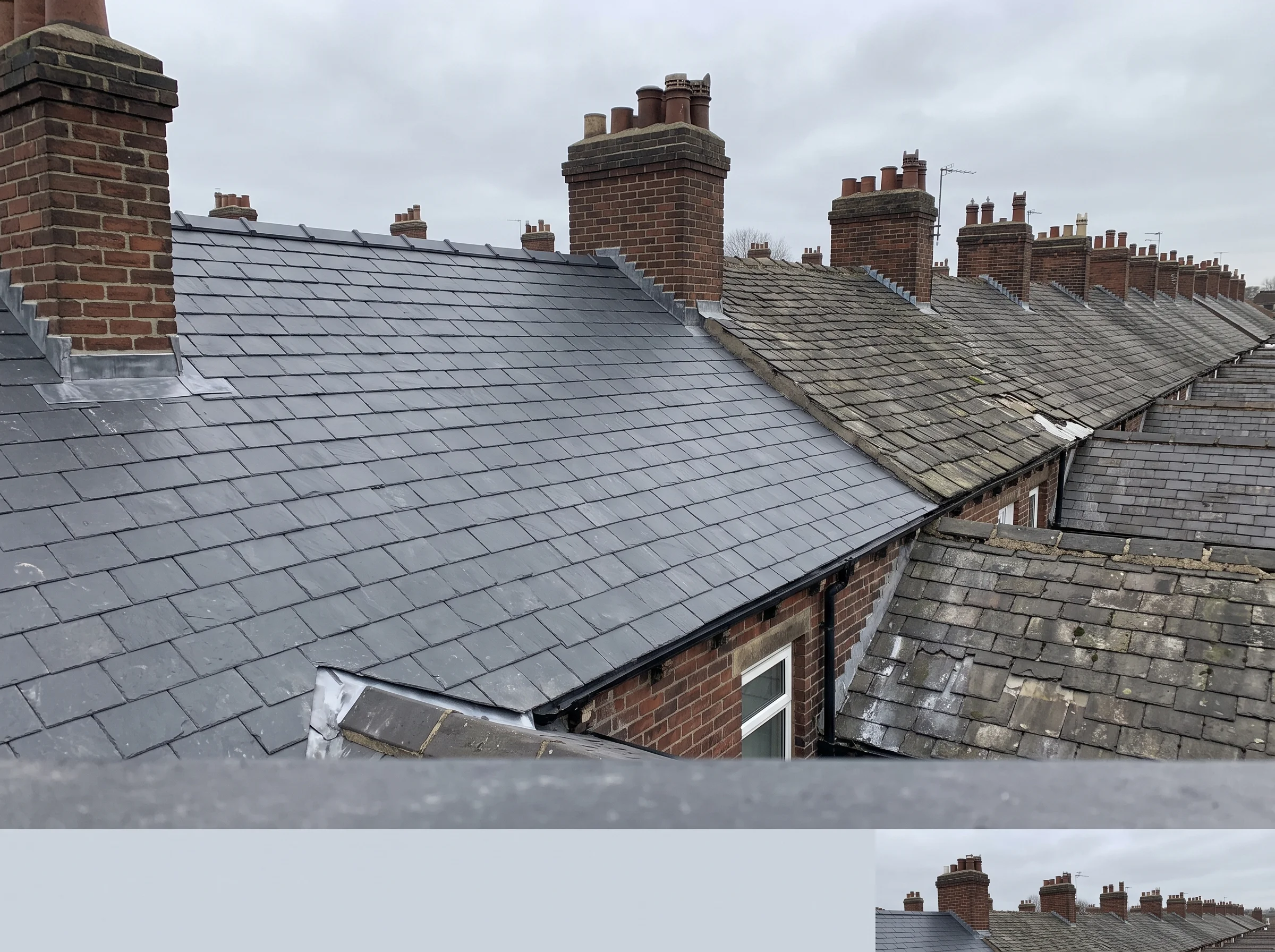 Newly re-slated terrace roof with dark uniform courses beside older weathered rooflines